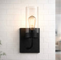 The Zephyr matte black wall sconce with clear glass shade on white tile – lit