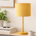 The Solara ochre linen table lamp lit on a bedside table next to a linen headboard