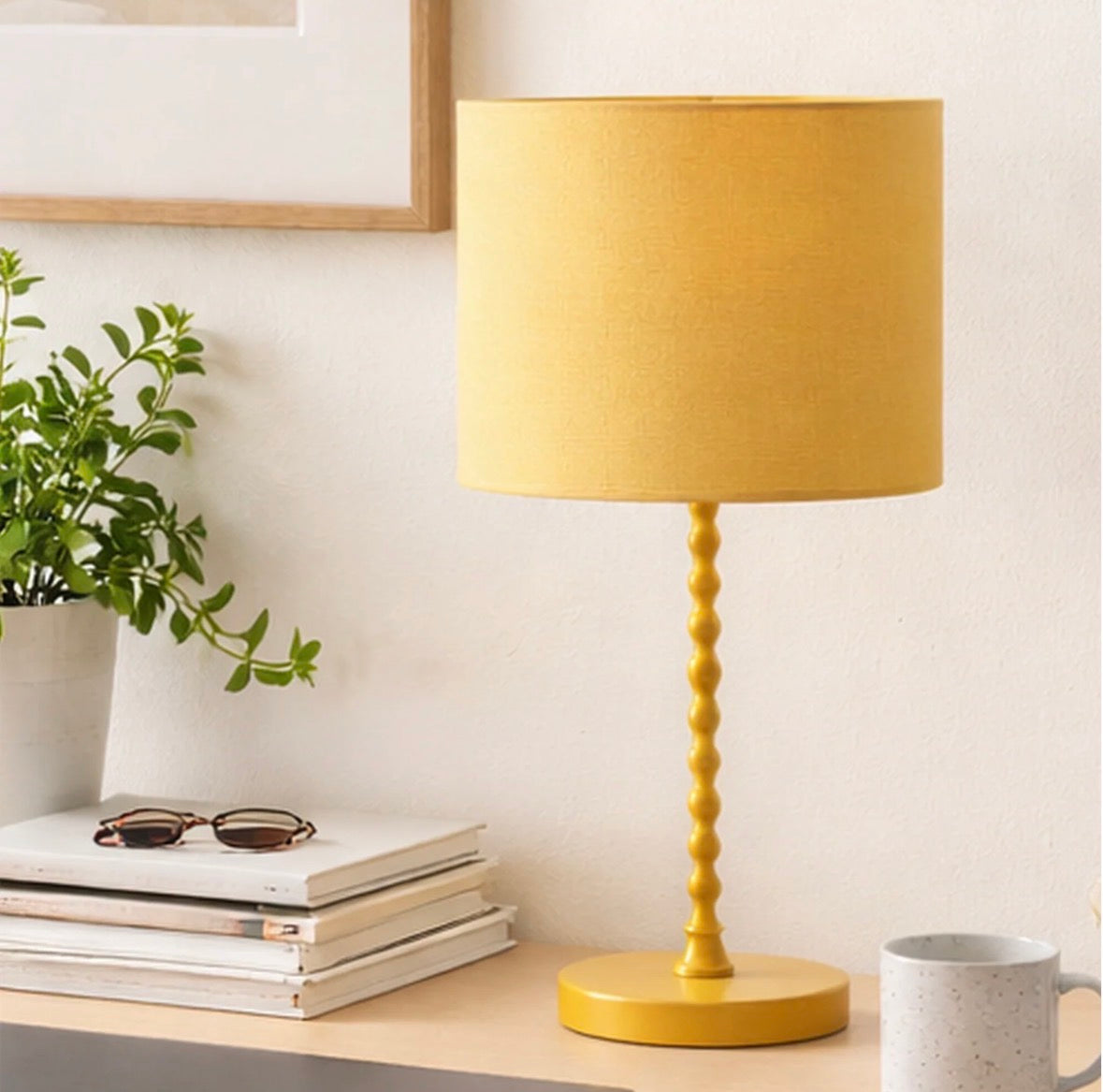 The Solara ochre linen table lamp lit on a bedside table next to a linen headboard