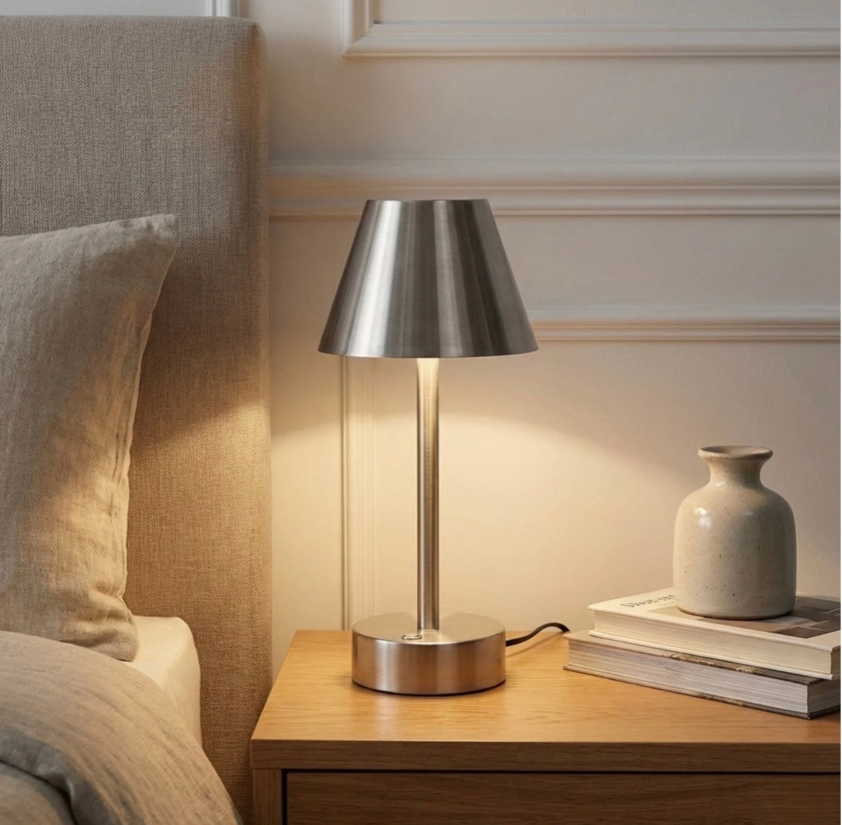 The Lumière brushed nickel cordless LED table lamp lit on a wooden nightstand – warm glow