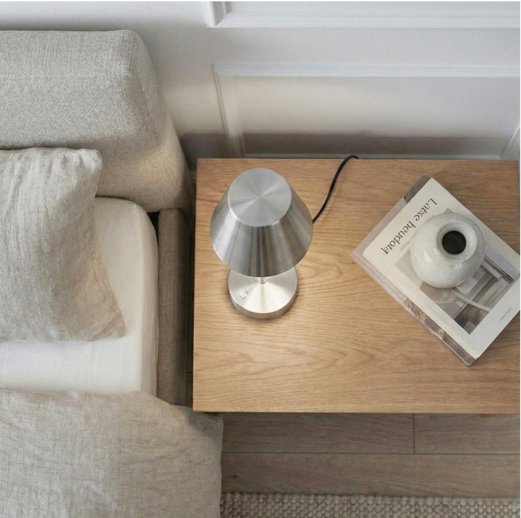 The Lumière brushed nickel table lamp – overhead view on nightstand next to sofa