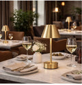 The Aurelia cordless brass LED table lamp on a marble restaurant dining table