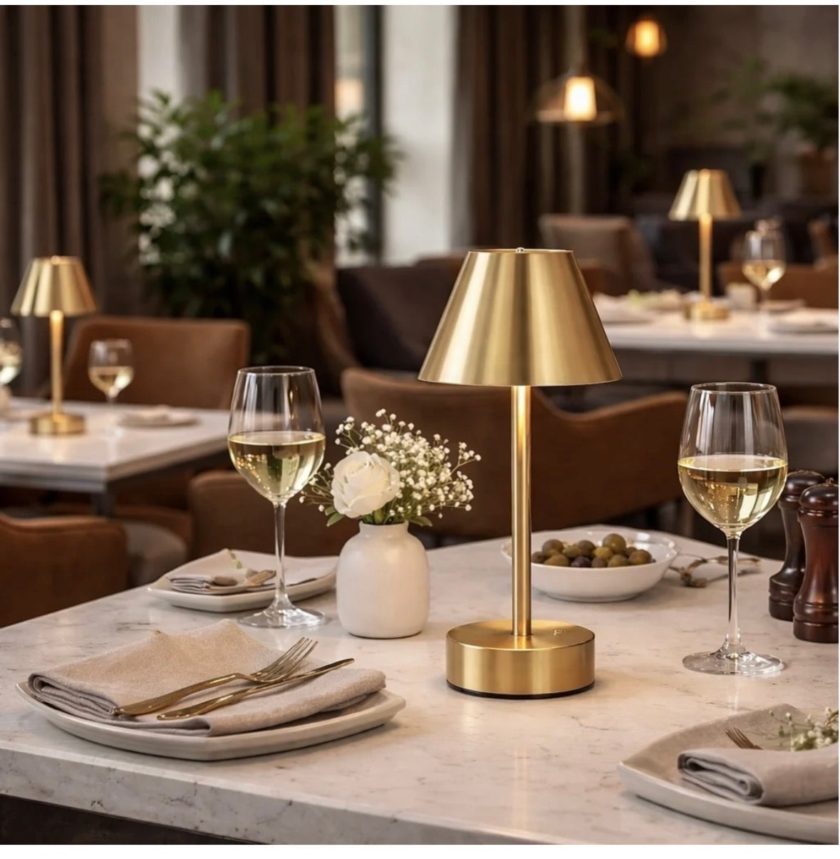 The Aurelia cordless brass LED table lamp on a marble restaurant dining table